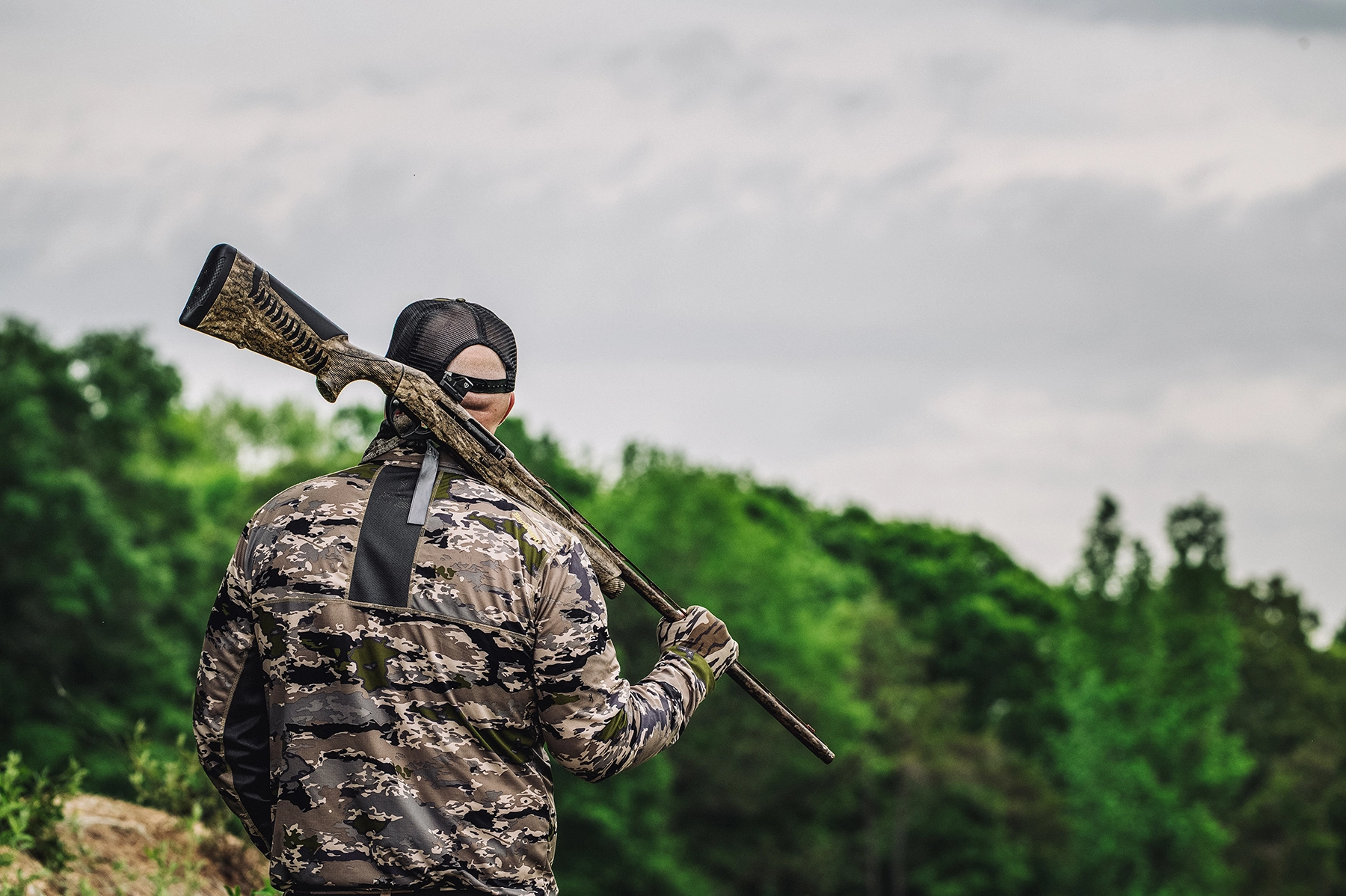 a turky hunter holds his shotgun over his shoulder by the barrel