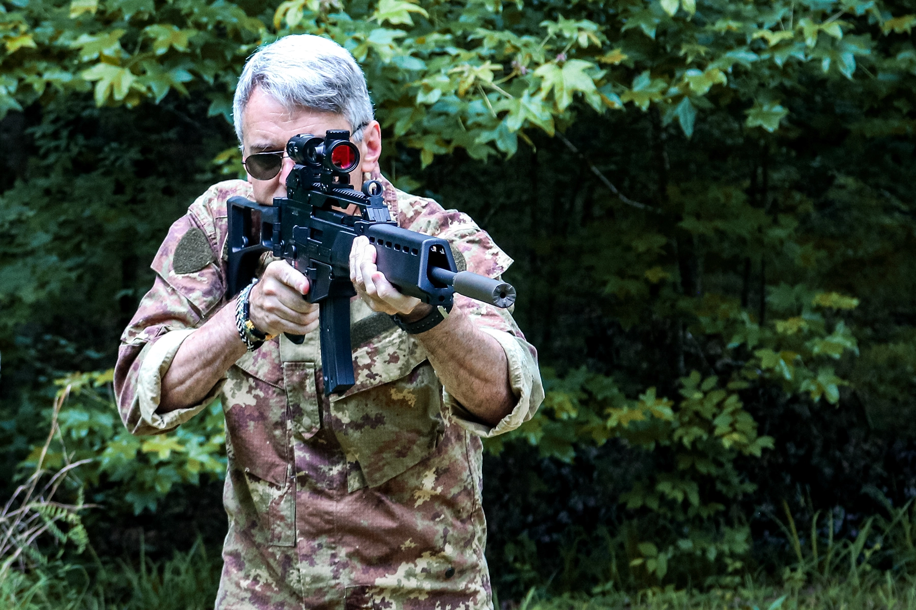 The author aiming the HK G-36 rimfire outfitted with a red dot, magnifier, and suppressor