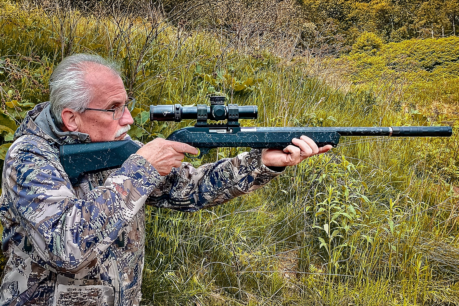 the author aiming the Ruger 10/22 Carbon Fiber rifle with a Trijicon Credo HX 1-8x28 riflescope and a SilencerCo Switchback suppressor