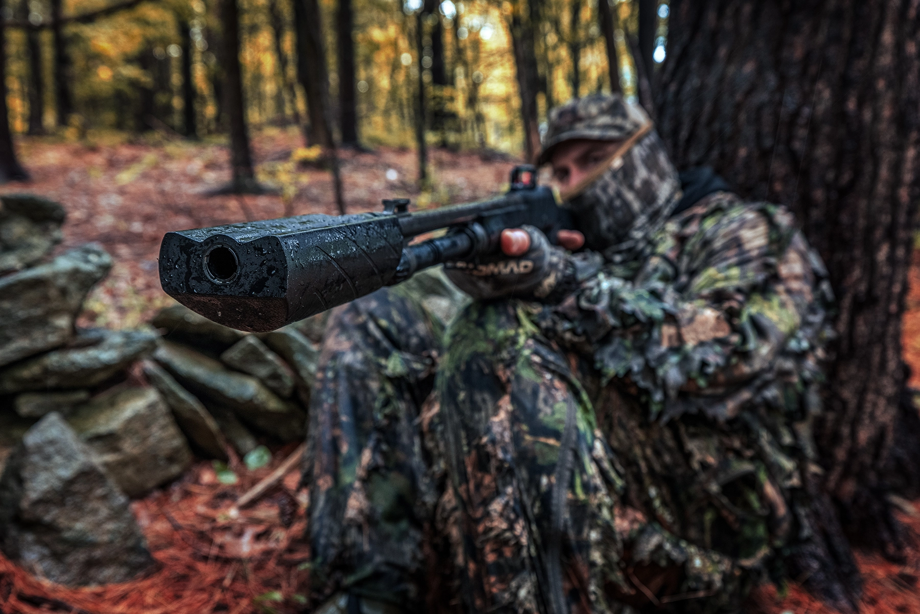 a turkey hunting aiming a shotgun with a red dot sight and a Banish 12 suppressor attached