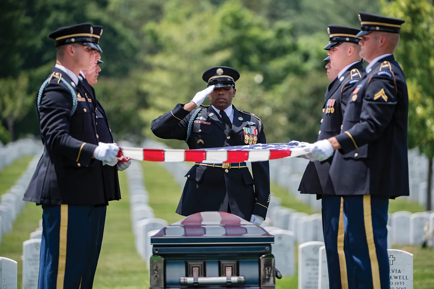 US Army soldiers folding an American flag over a casket at a veteran's cemetery.