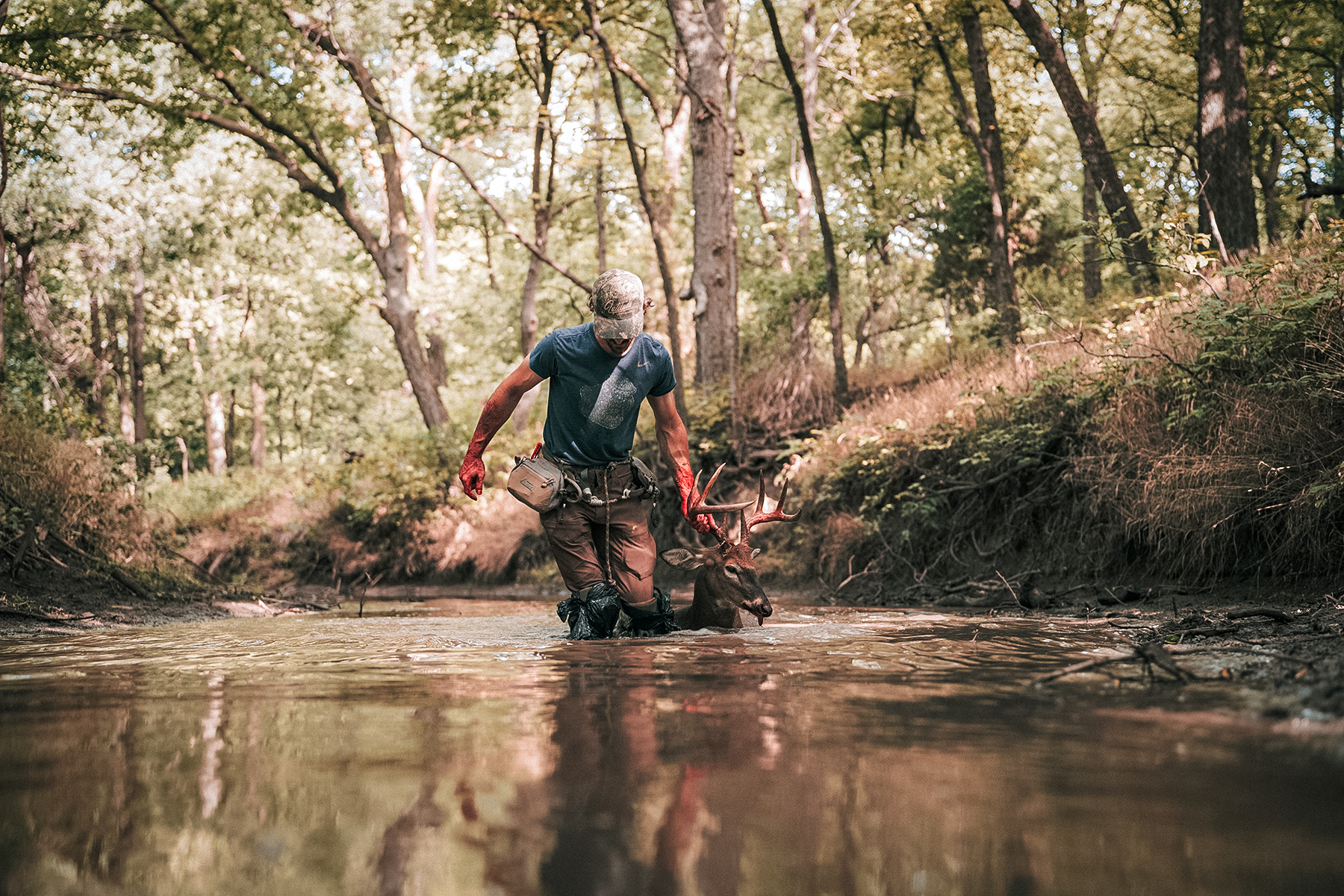 a hunter dragging a buck through a stream