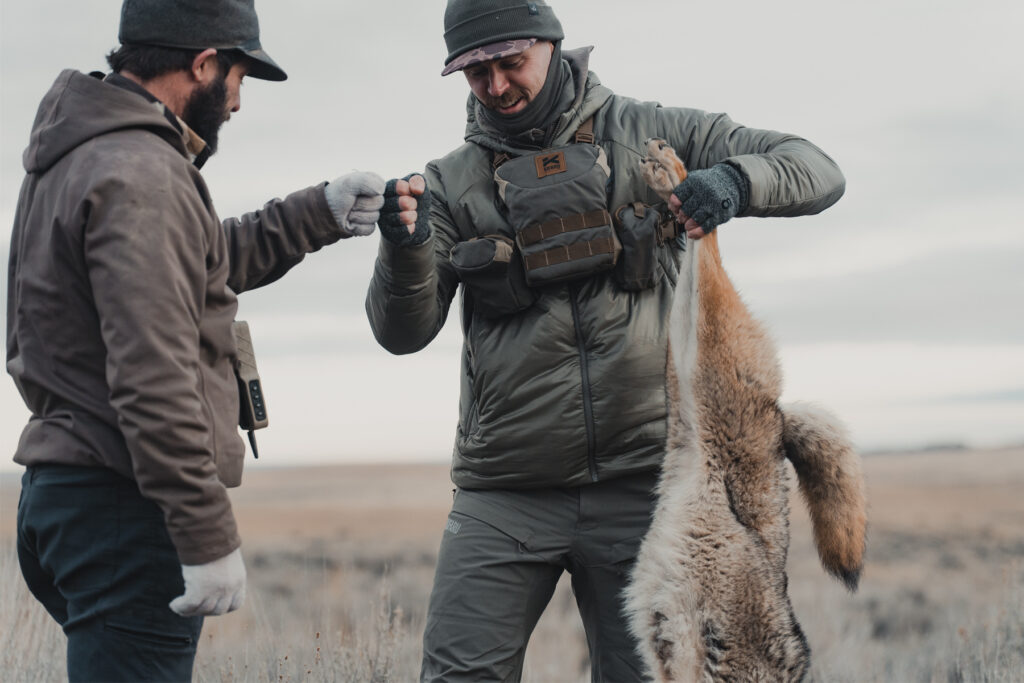 A hunter holds up a predator on an open prairie.