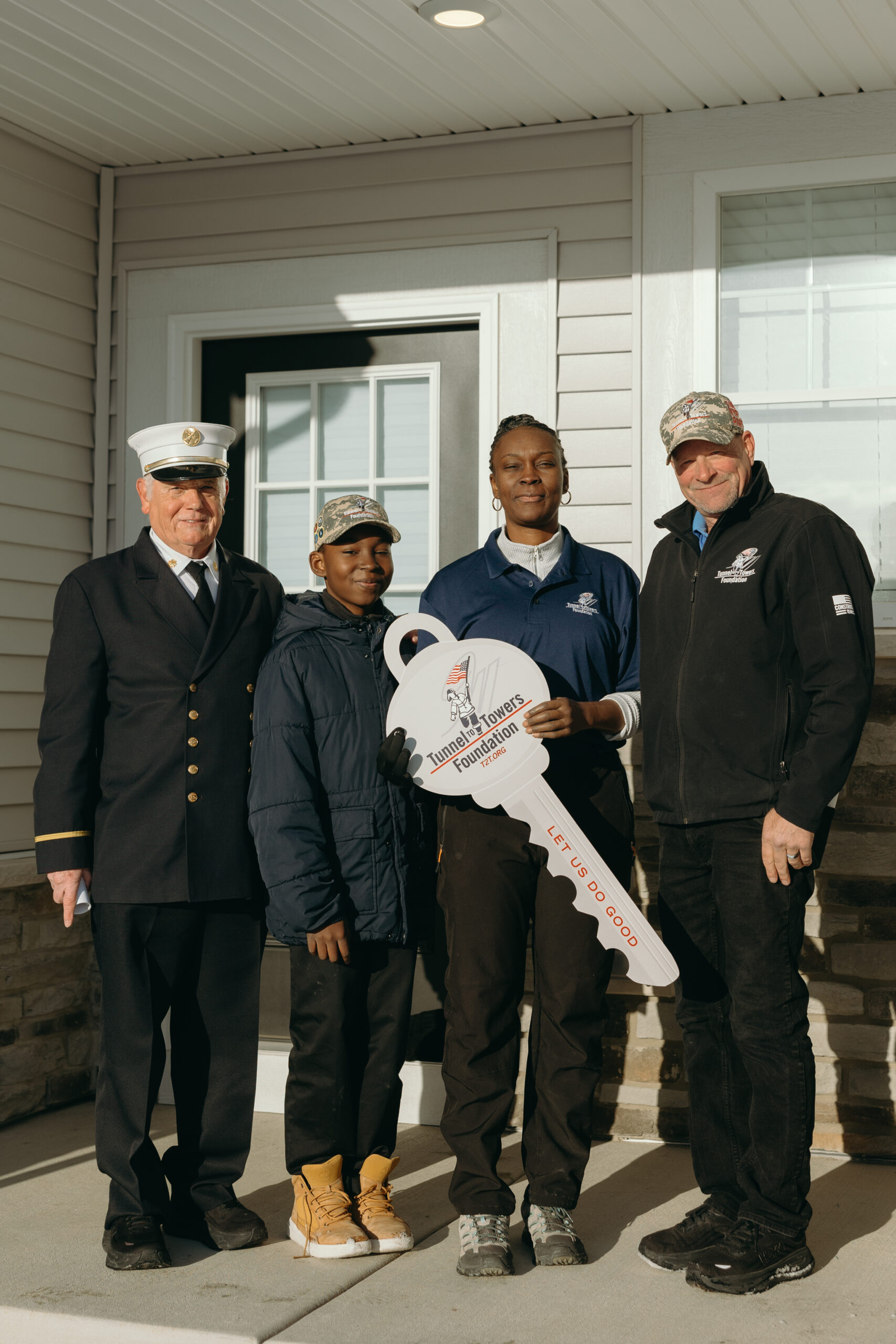 A woman holds a large key and stands with her son and Tunnel to Towers representatives in front of a house.
