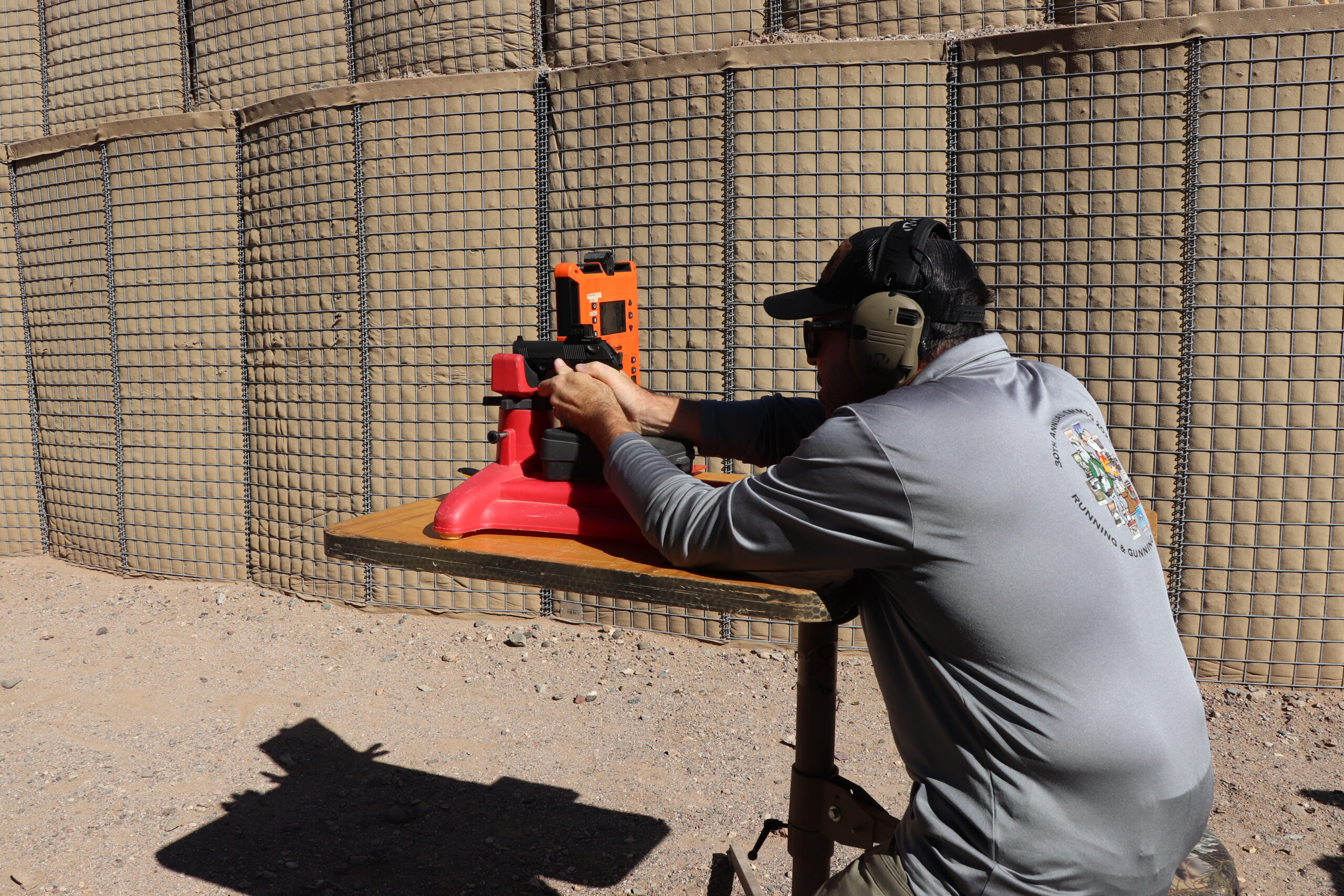 A man sits at a shooting bench and fires a pistol.