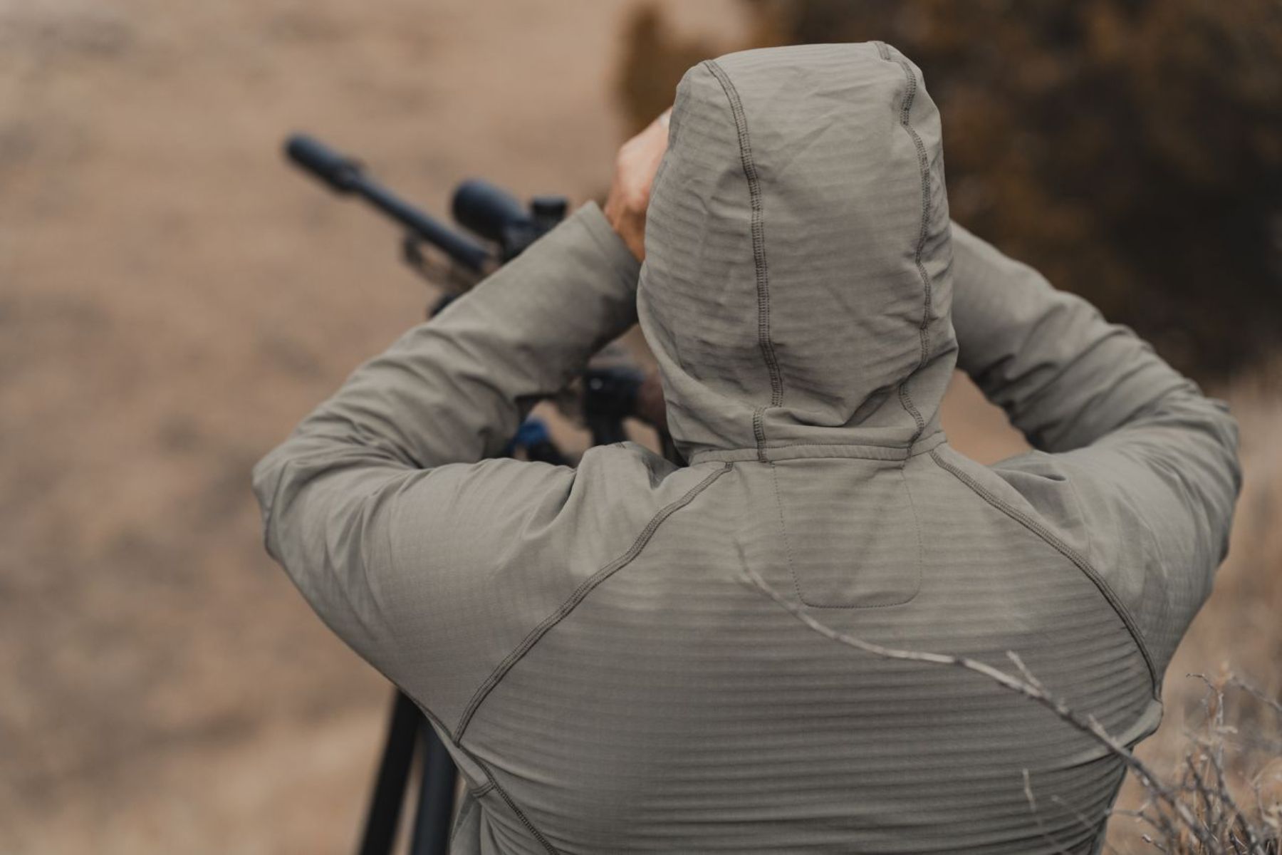 A man in a Kifaru grid Fleece hoodie looks through binos.