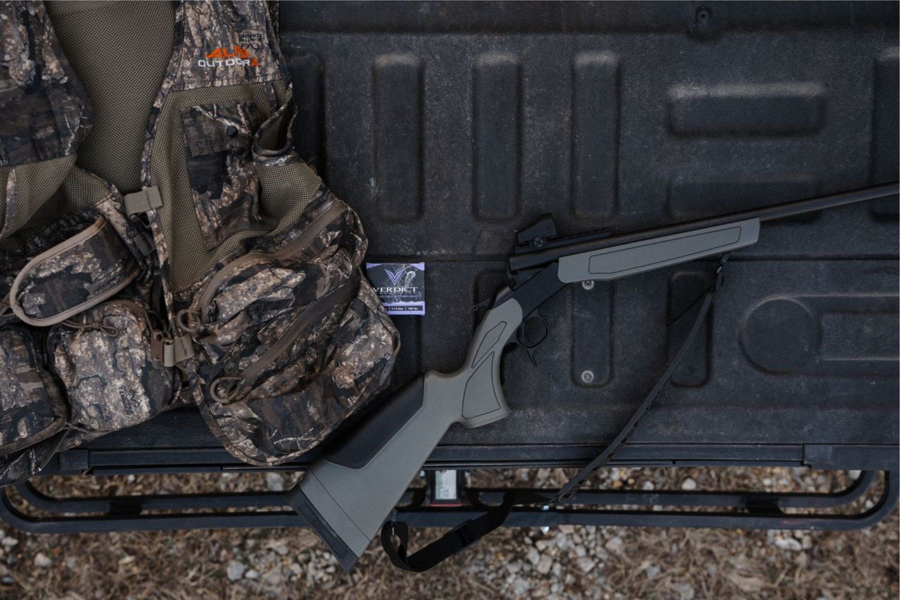 A CVA Spur shotgun sits on the tailgate of a truck next to a camo turkey vest.