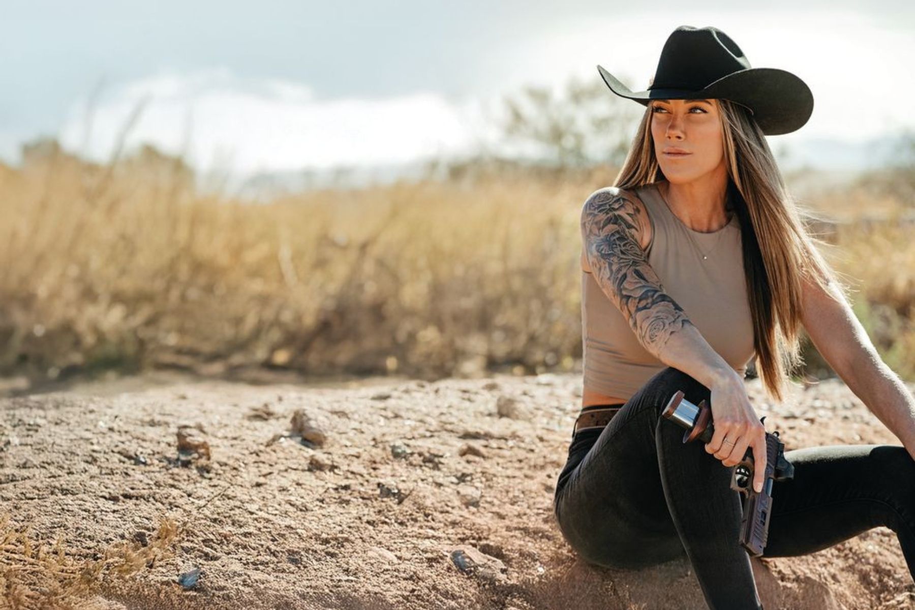 A woman in a cowboy hat sits in the dirt. 