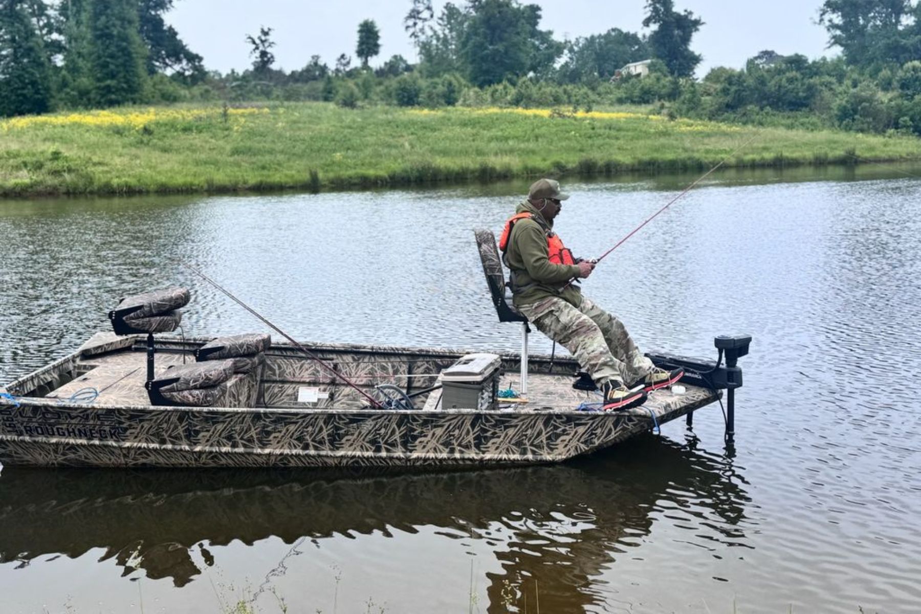 Steve Harvey sits in a flat bottom boat and holds a fishing rod.