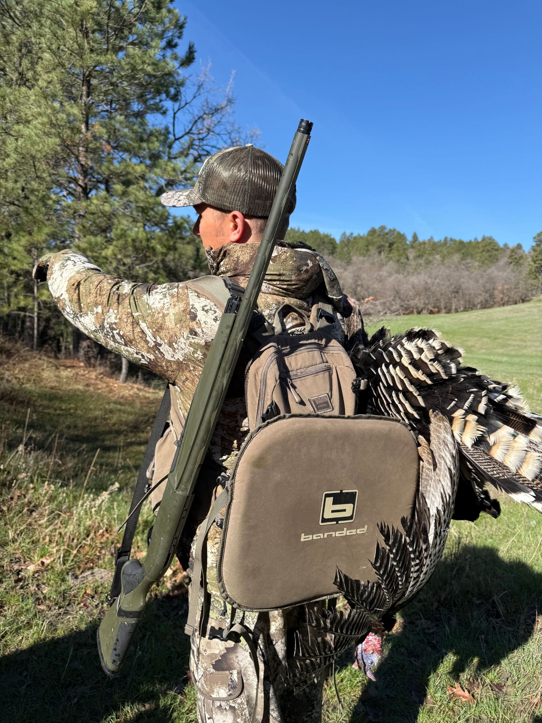 A man in camo carries a shotgun and a turkey