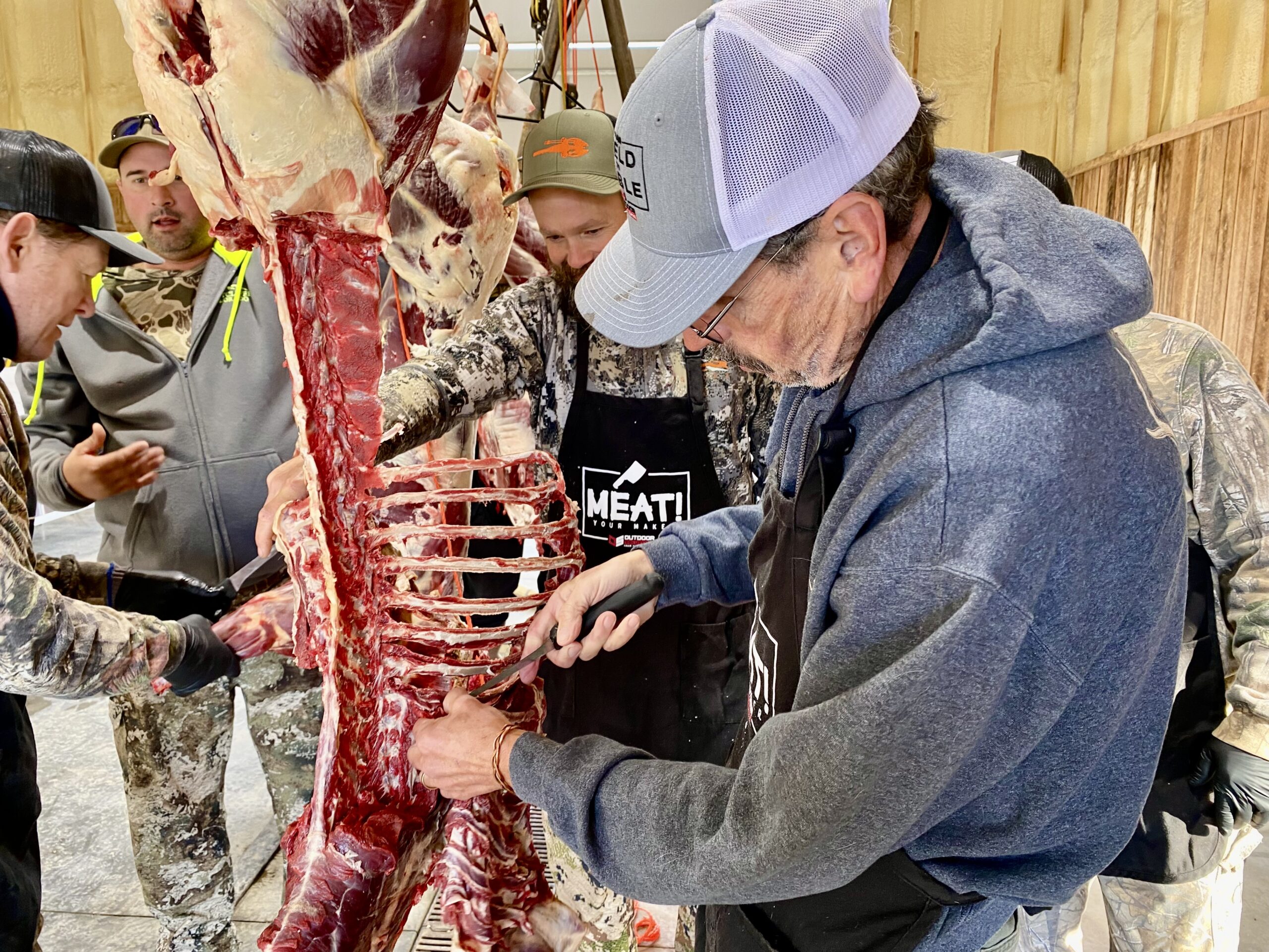 Several men butcher a hanging deer.