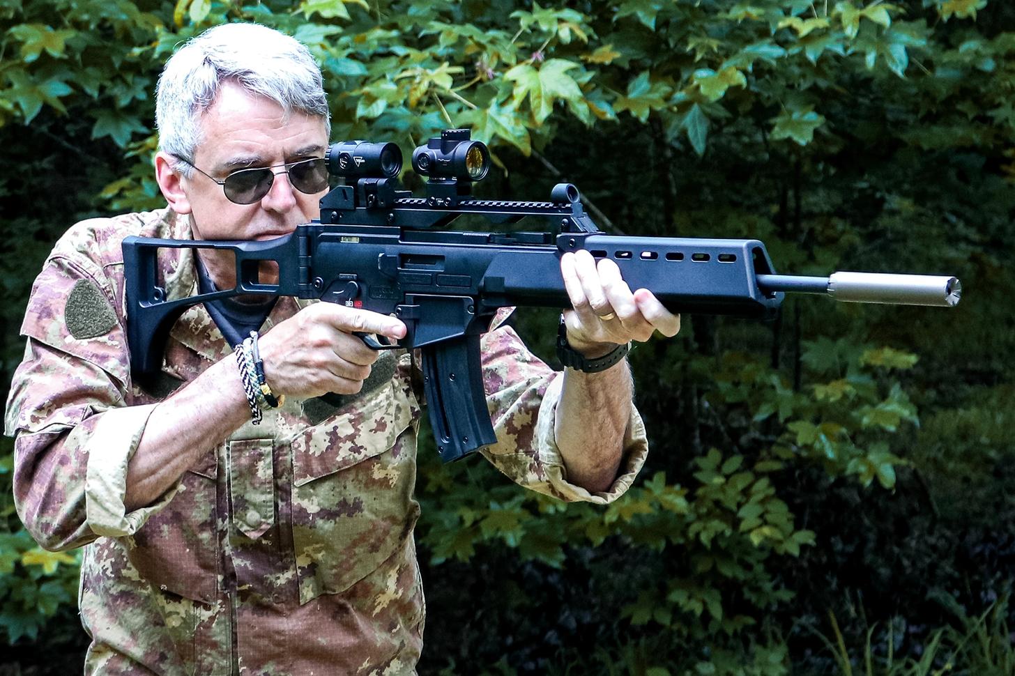 The author aiming the rimfire rifle outfitted with a red dot, magnifier, and suppressor