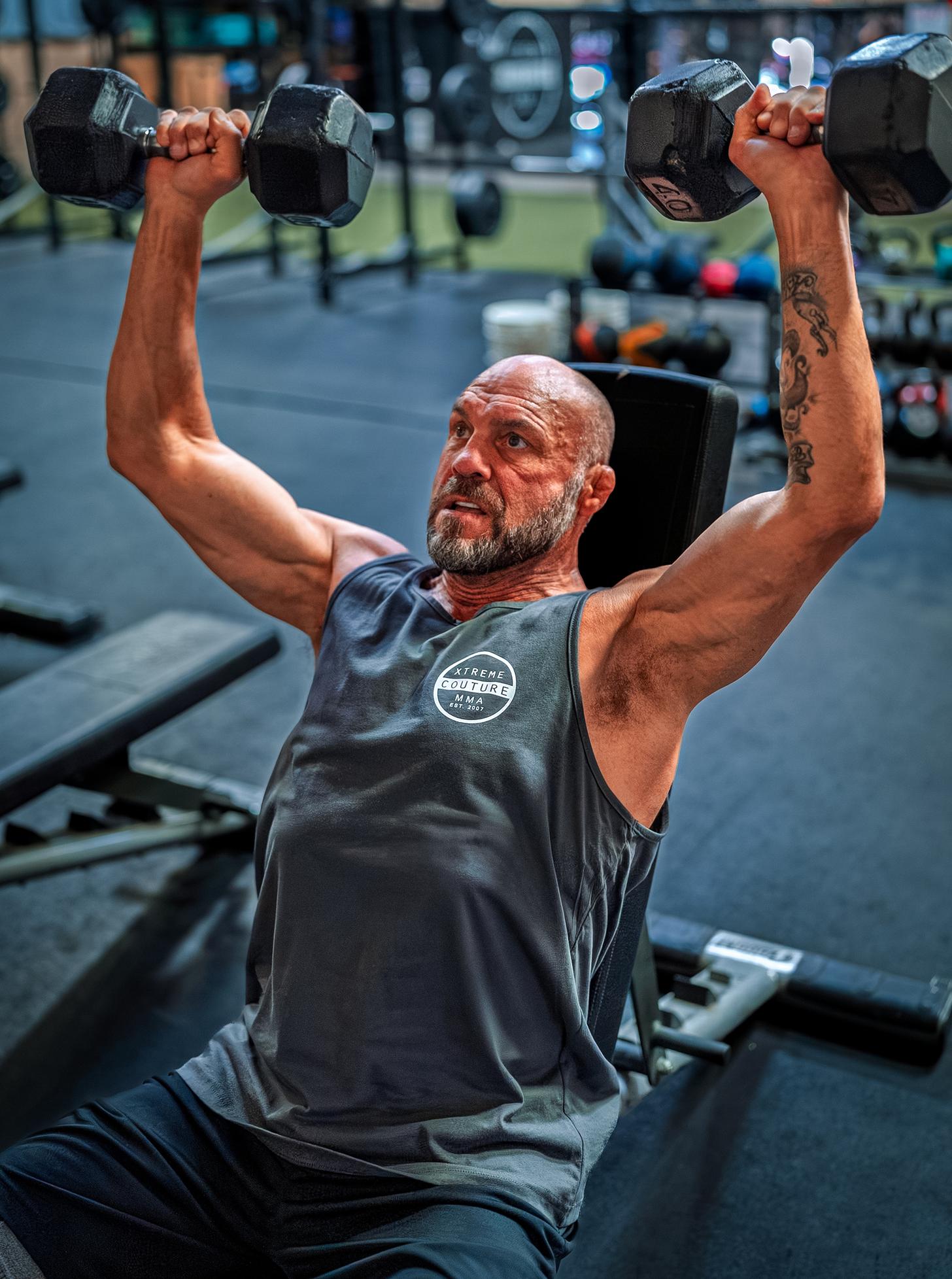 Randy Couture doing dumbbell shoulder presses in the gym