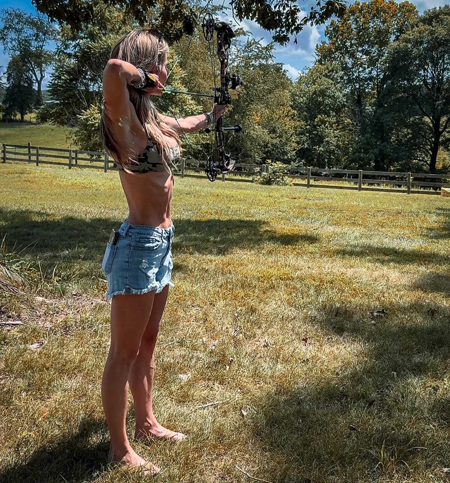 Lauren Brown shooting a compound bow in a large yard