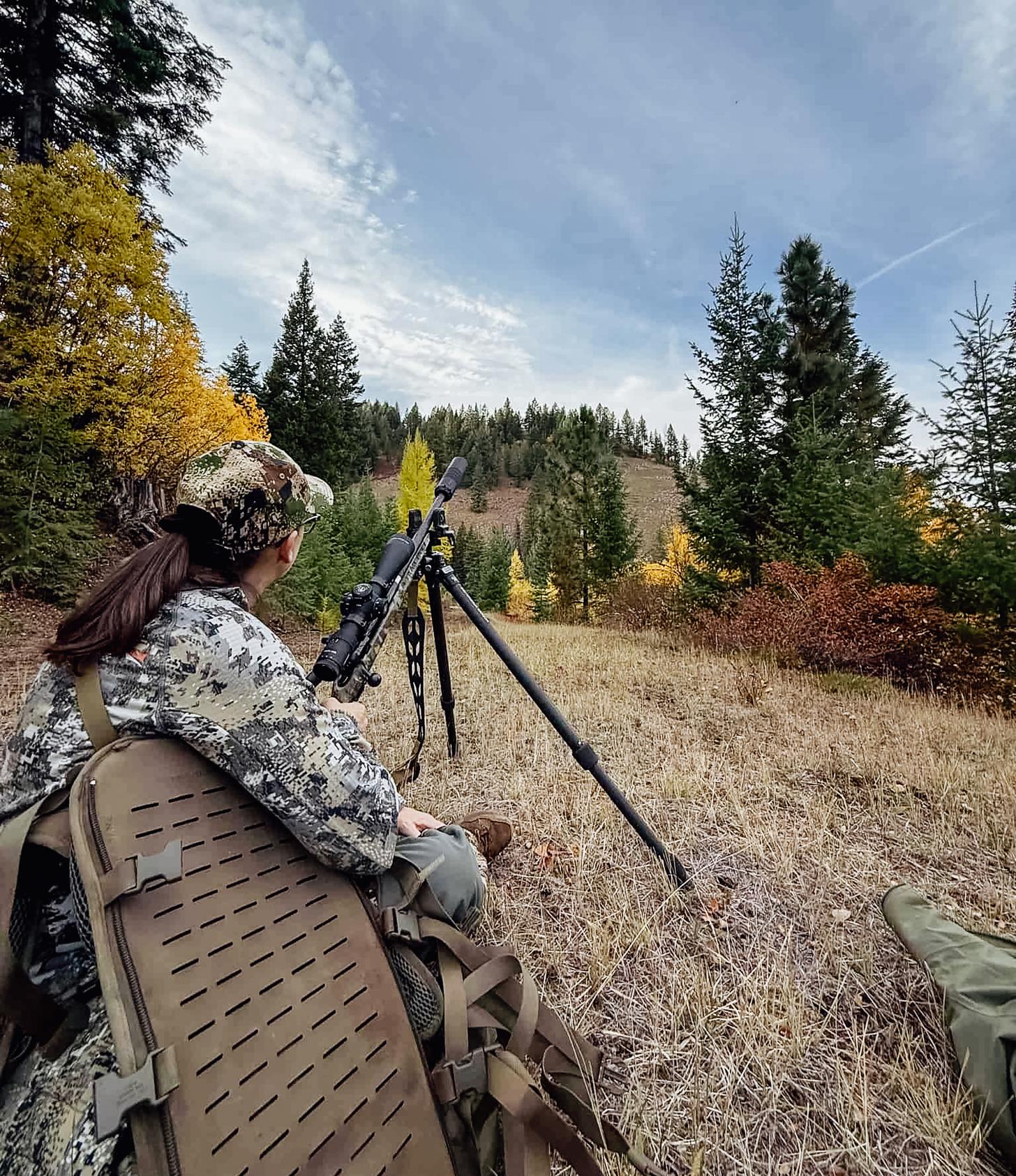 hunter scanning the hill with rifle on a tripod