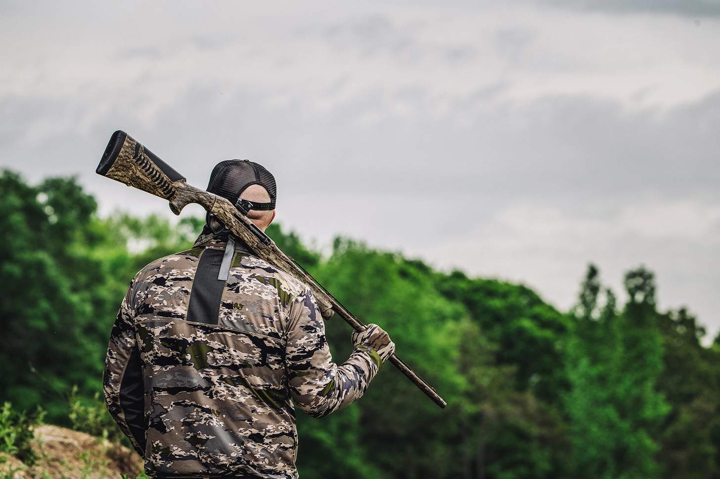 a turky hunter holds his shotgun over his shoulder by the barrel