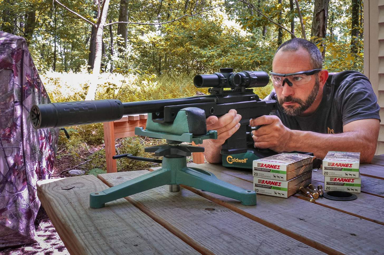a man shooting a suppressed hunting rifle from a rest with boxes of ammo in foreground
