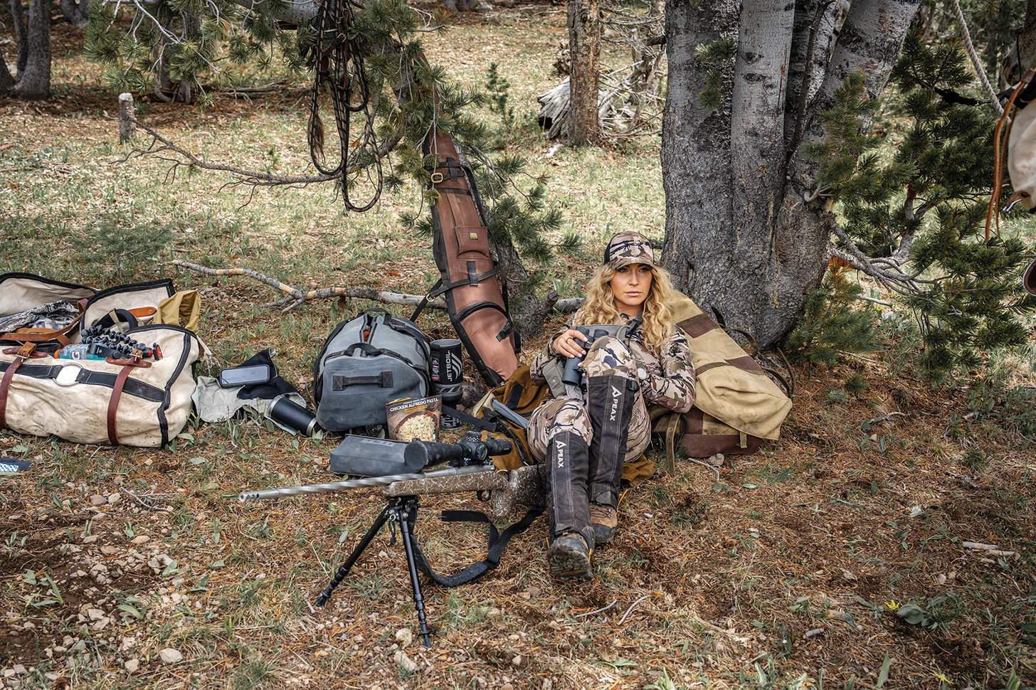 glassing beneath a tree with a rifle on a bipod