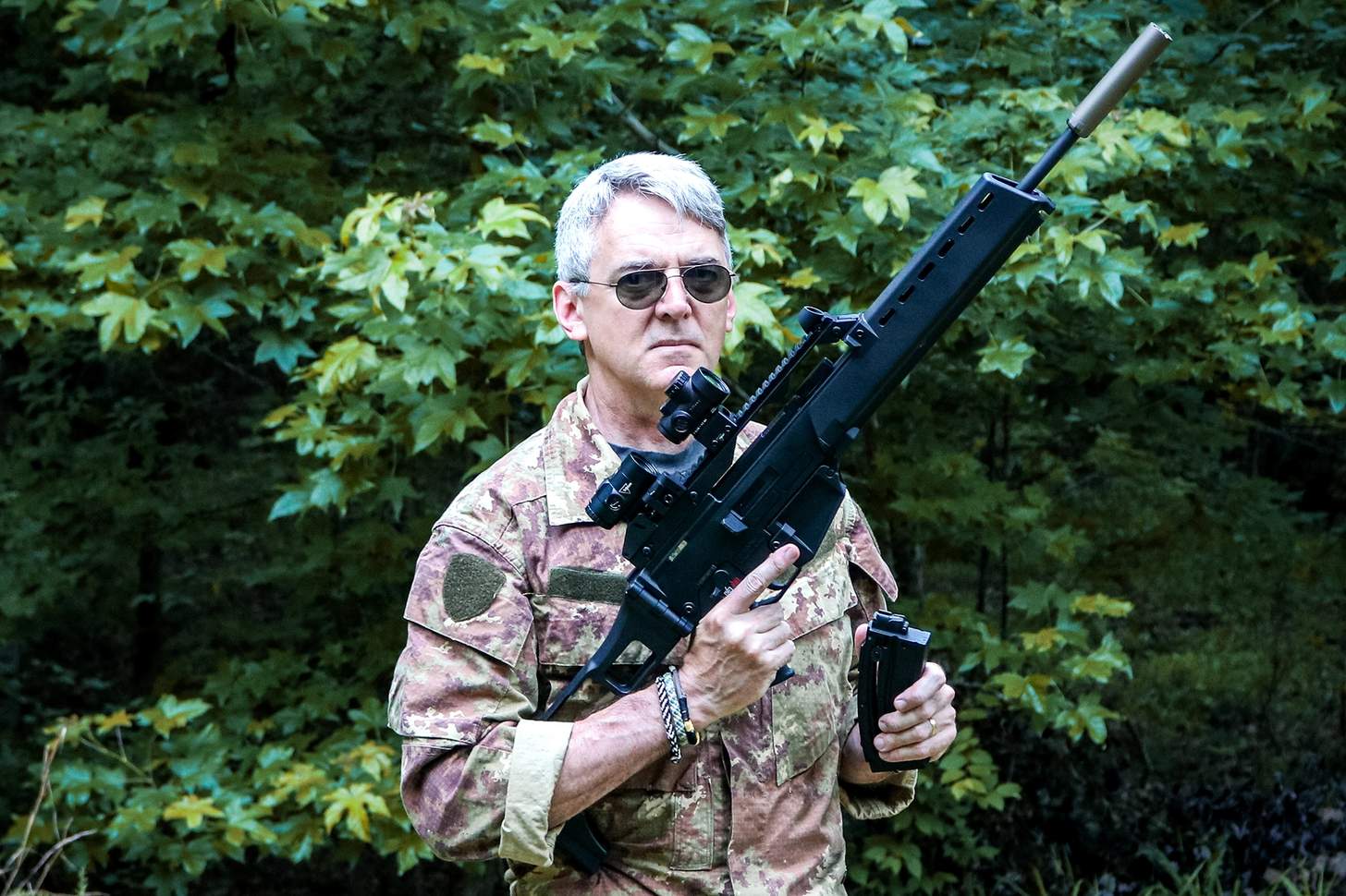 The author holding the HK G-36 rimfire outfitted with a red dot, magnifier, and suppressor