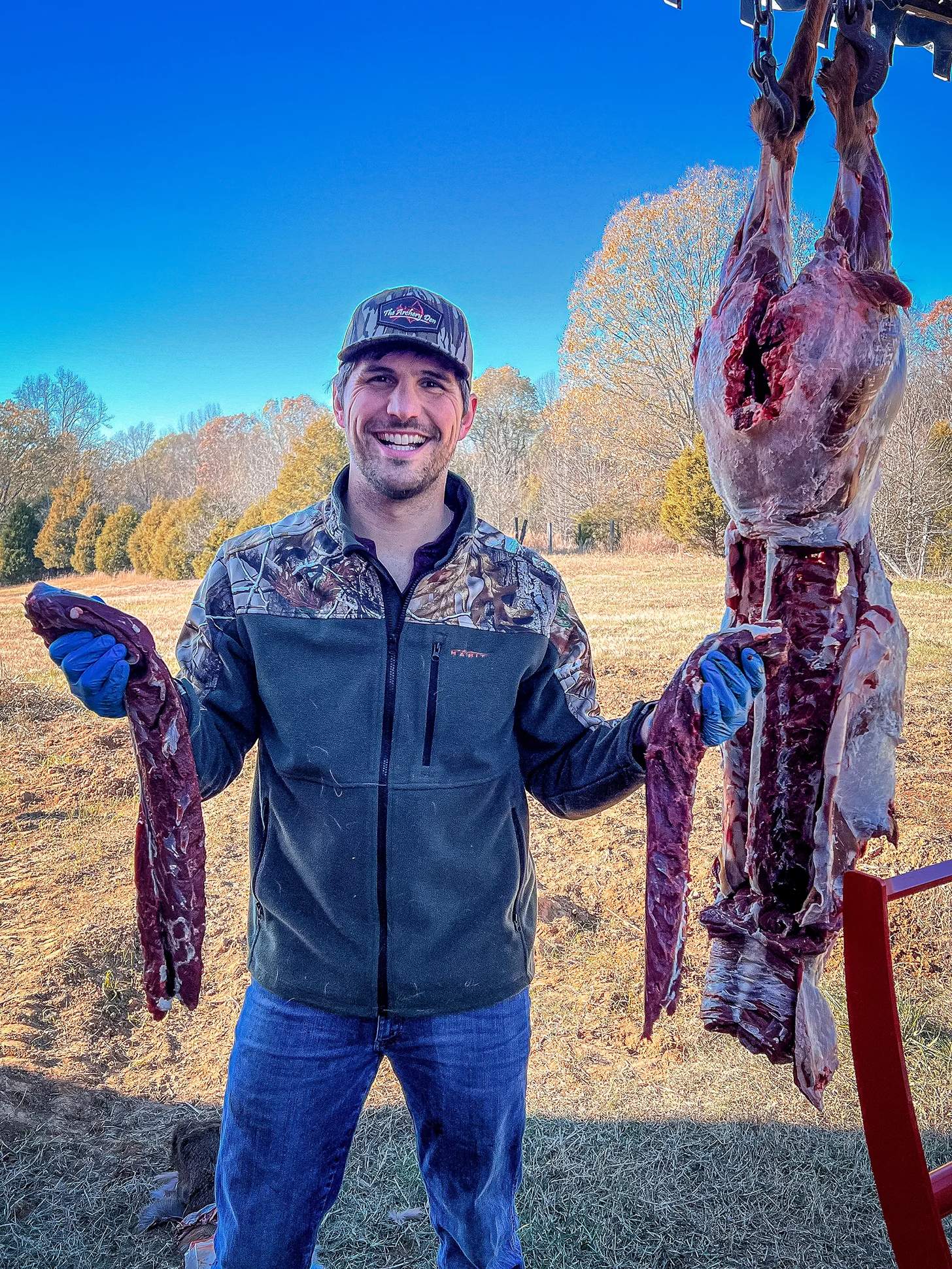 Justin Adams holding two venison backstraps next to a partially butchered deer