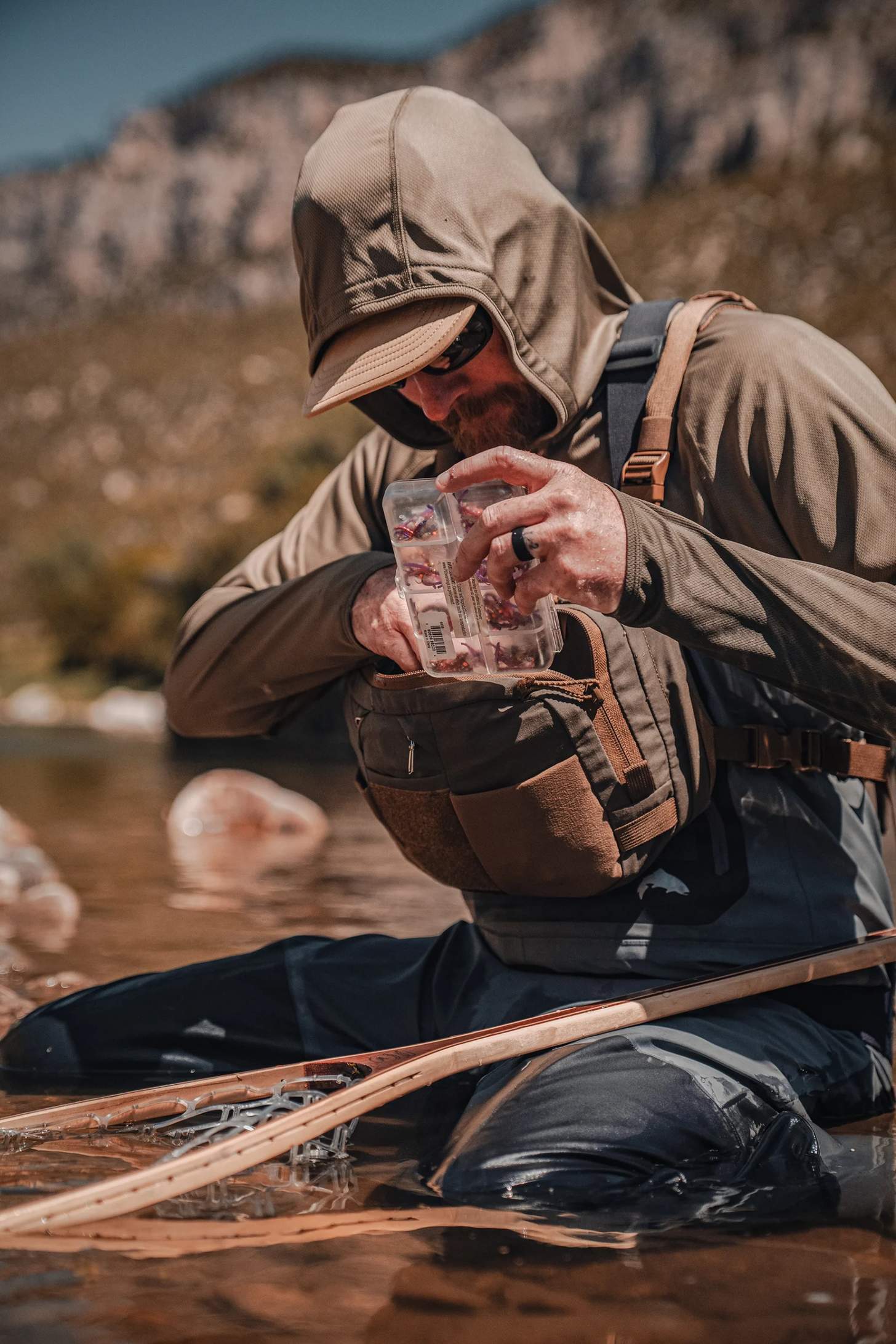 a fly angler wearing the Kifaru Steelhead Chest Rig with the Kifaru Hydro Harness kneeling with a fly box