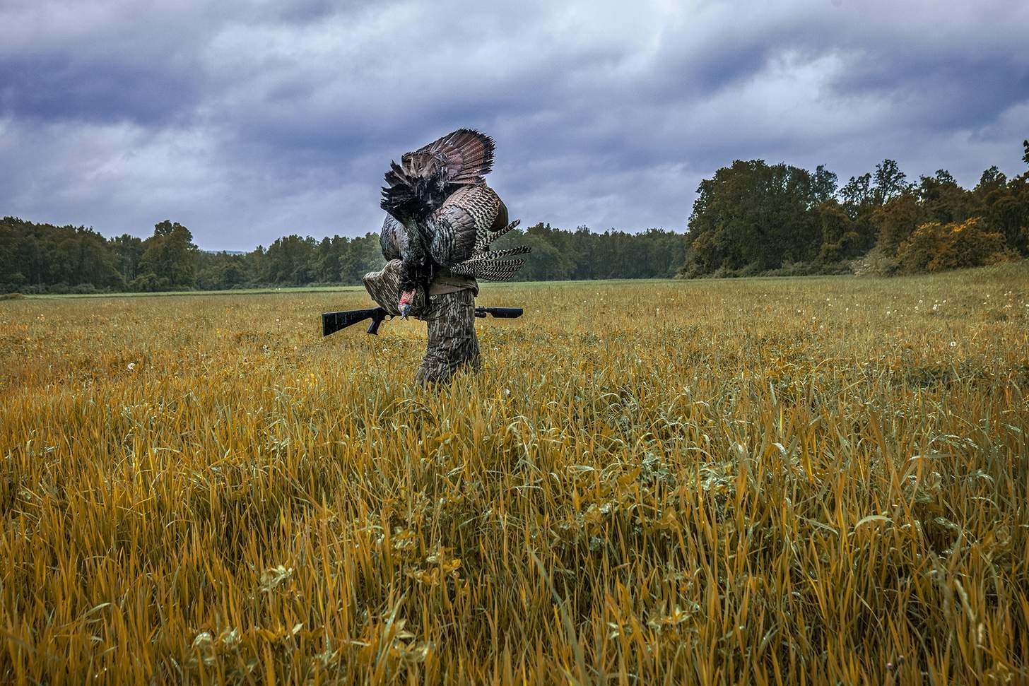 hunter carrying a dead turkey and a shotgun with a Banish 12 suppressor attached