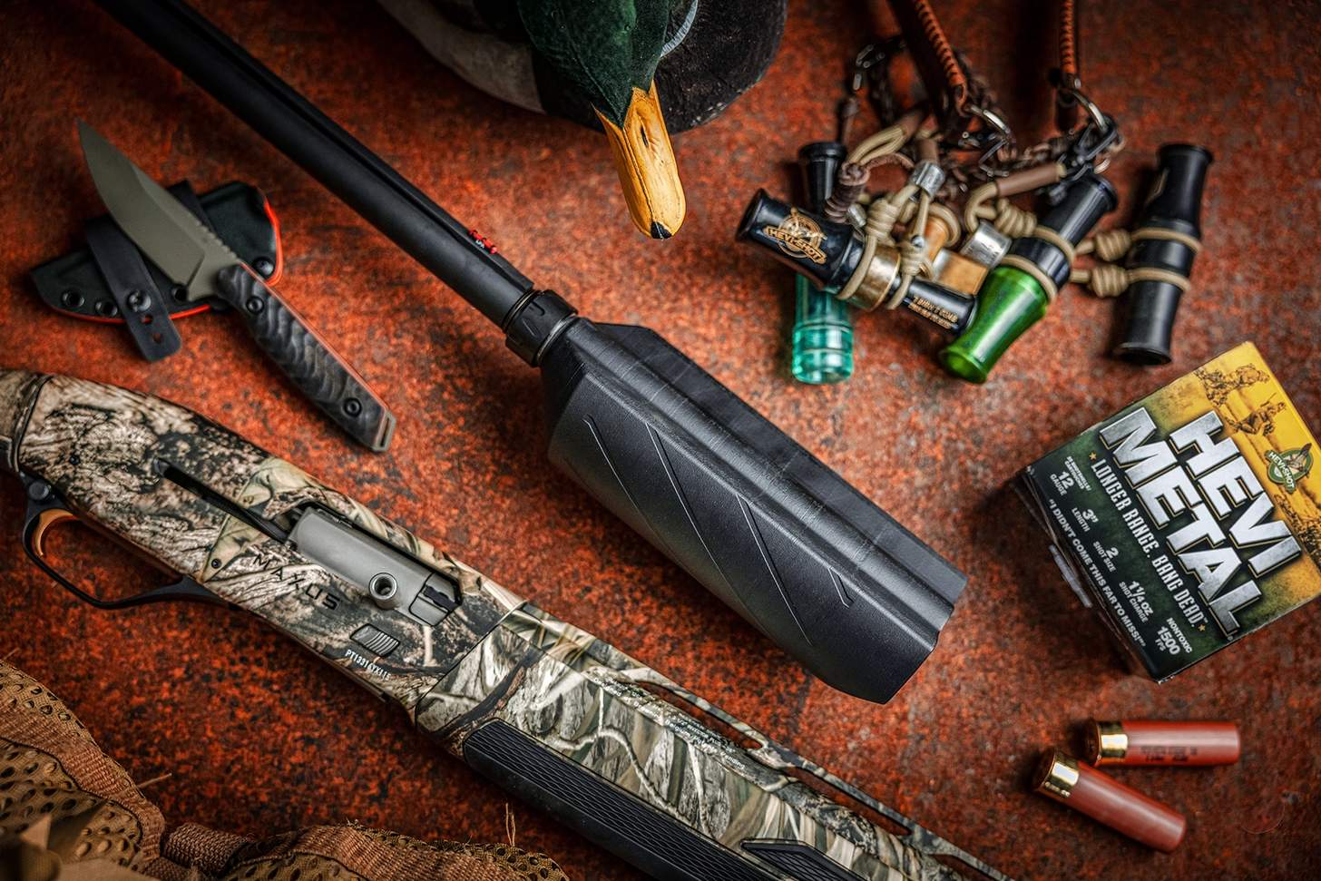 suppressor attached to a muzzle with a semi-auto camo shotgun, ammo, and duck calls