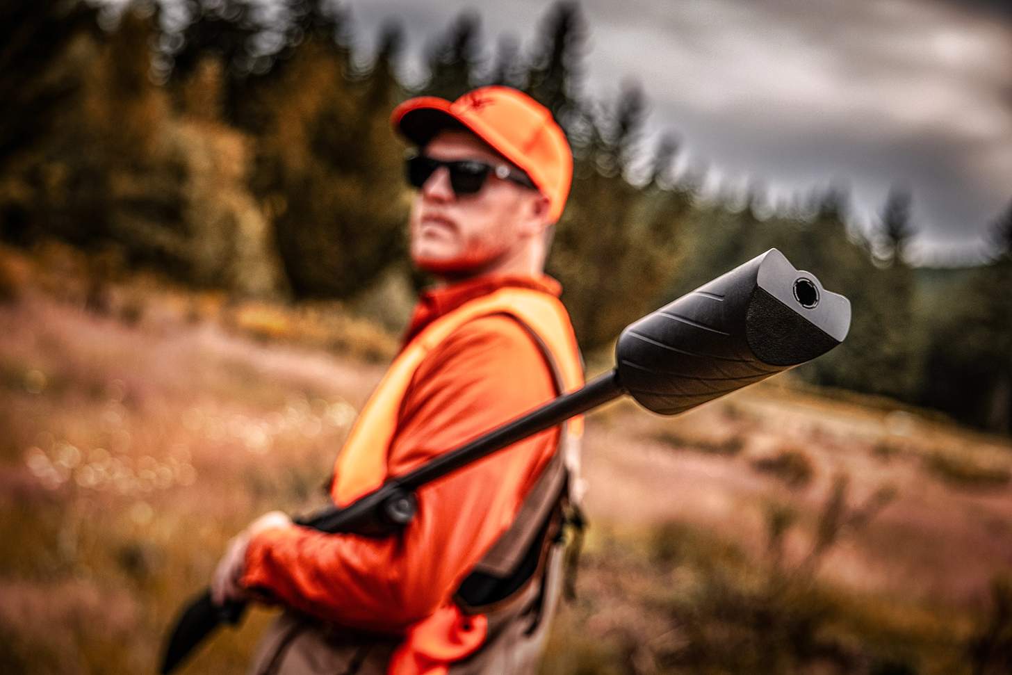 The Banish 12 shotgun suppressor on the muzzle of a shotgun being carried by a hunter in orange