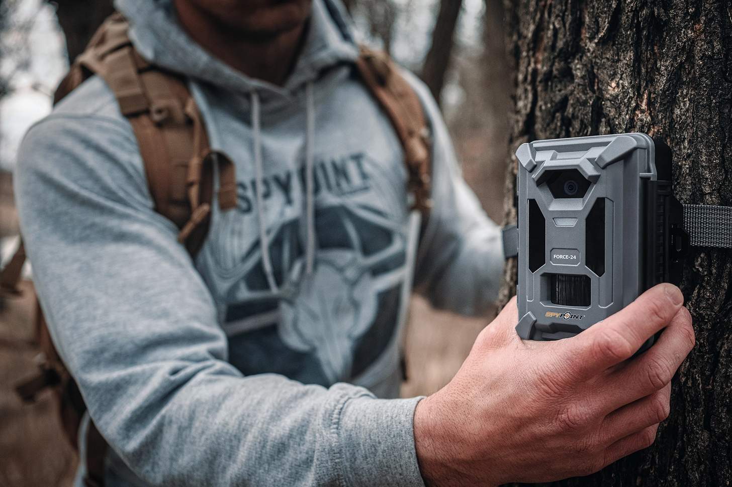 a man affixing a Spypoint FORCE-24 trail cam to a tree