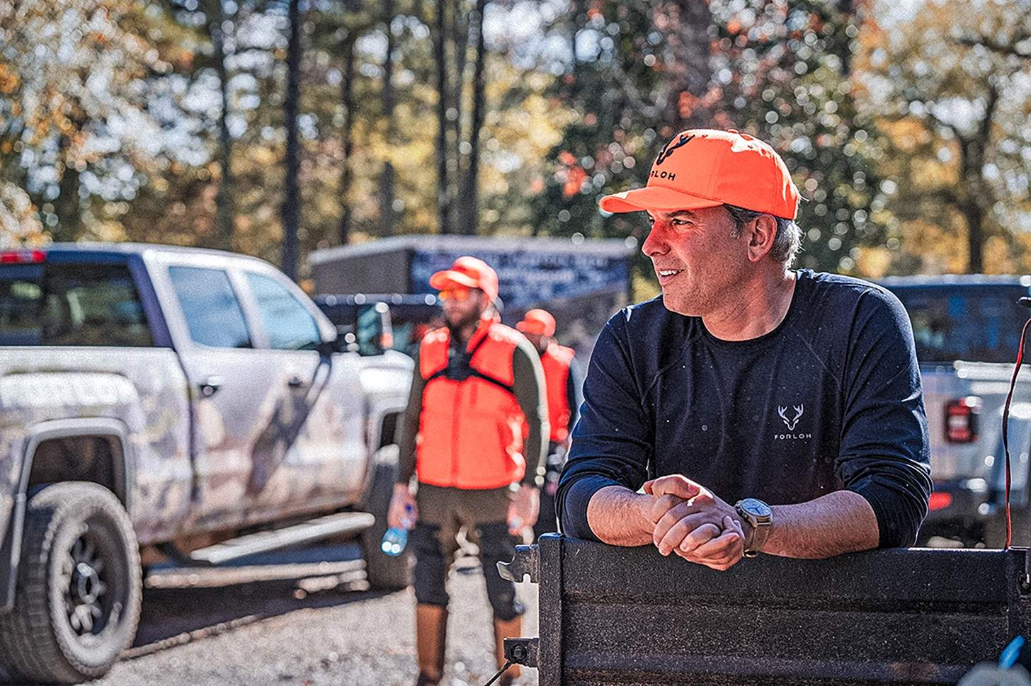 a man in a FORLOH hat and shirt leaning on a tailgate