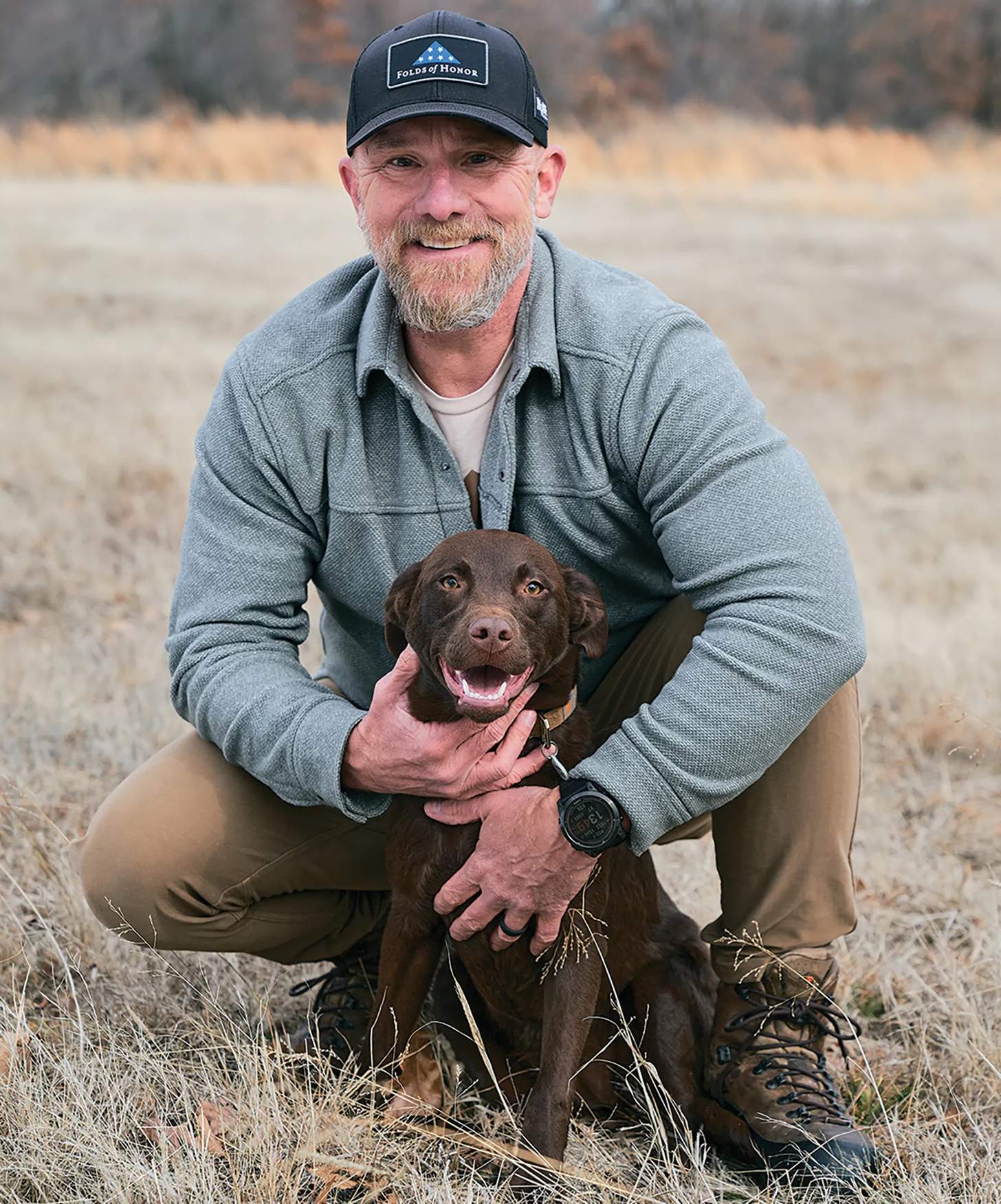 man with a dog in a field wearing a folds of honor hat