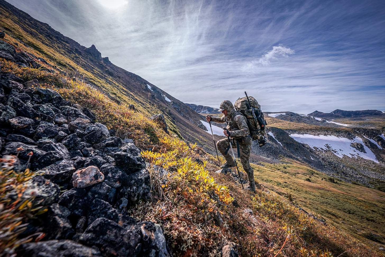 a hunter in kuiu gear climbing a steep hill with a heavy pack