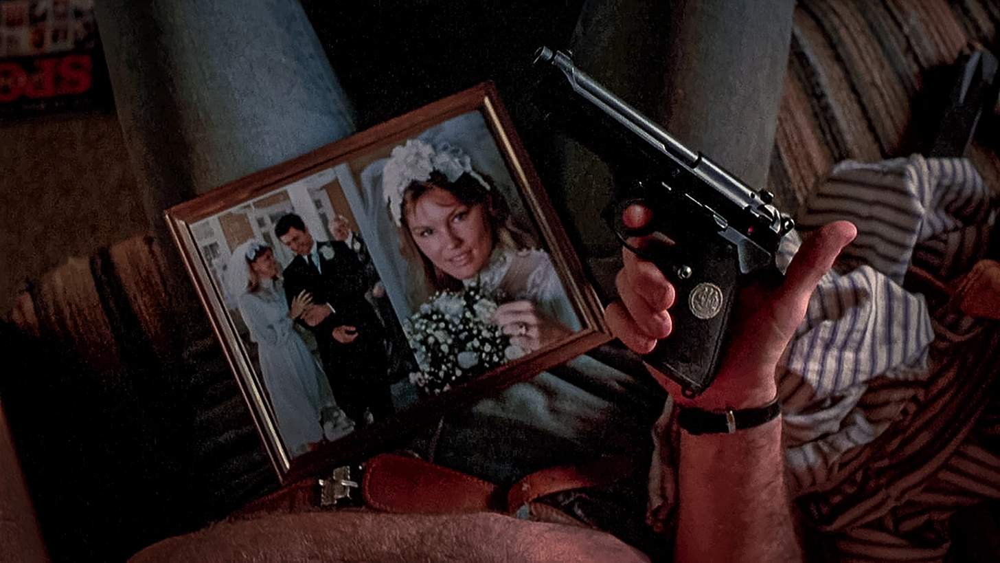 a man holding a Beretta 92F pistol next to a wedding photo