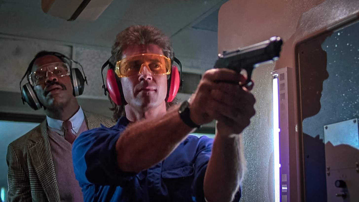 Sgt. Martin Riggs (Mel Gibson) shooting his Beretta 92F at the pistol range with Murtaugh (Danny Glover) behind him.