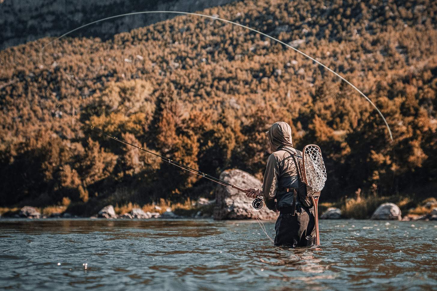 a man in a hoodie flyfishing in a mountain river