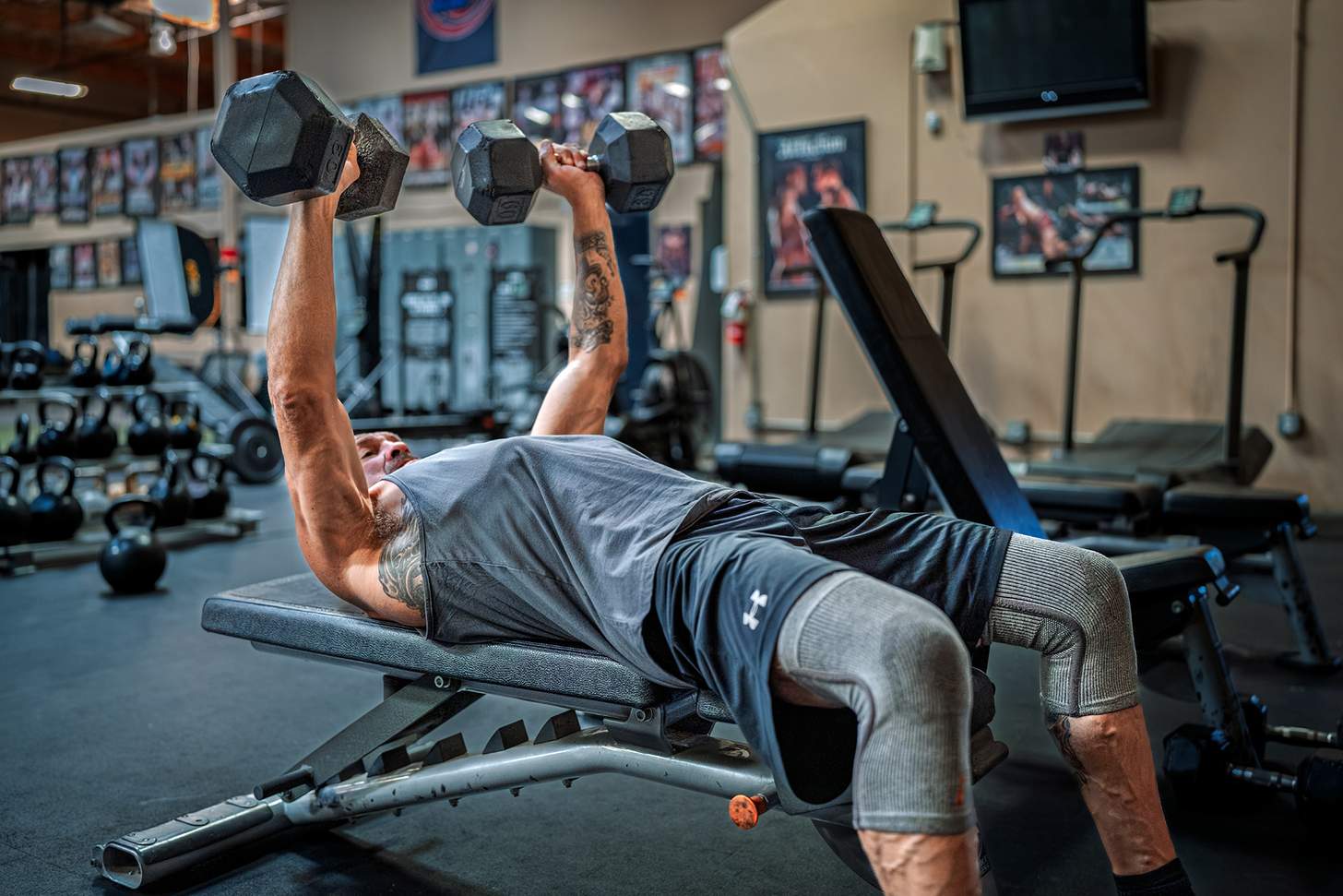 Randy Couture doing a dumbbell flat bench press in the gyme