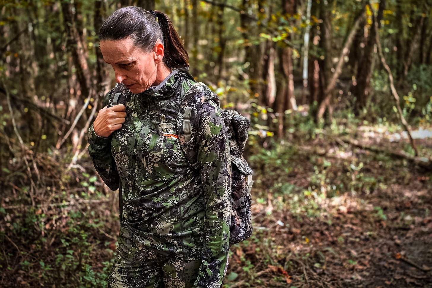 a female hunter walking through the woods in warm weather