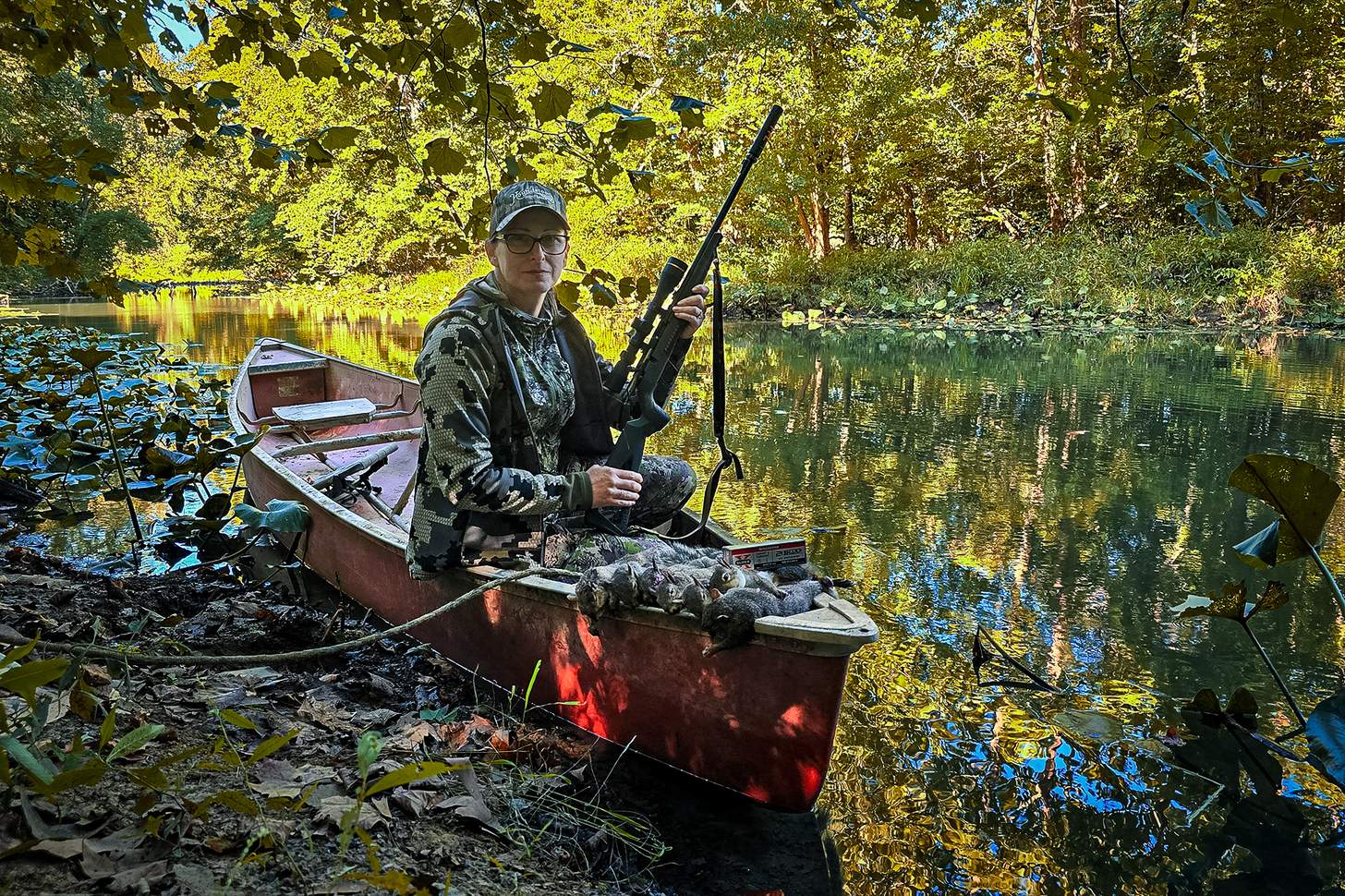 a hunter with a rifle in a canoe with dead squirrels
