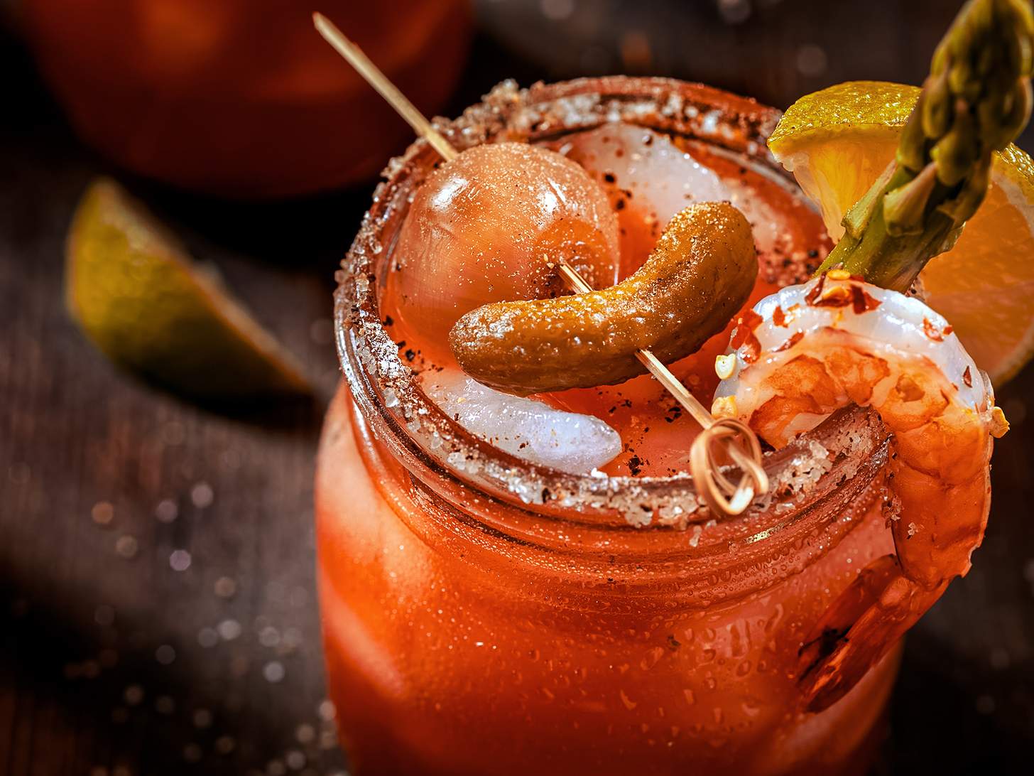 a bloody mary cocktail in a mason jar with a shrimp, asparagus, pickle, and onion