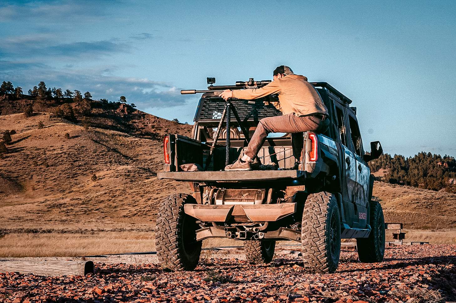 a man shooting a suppressed rifle from a tripod in an ATV bed