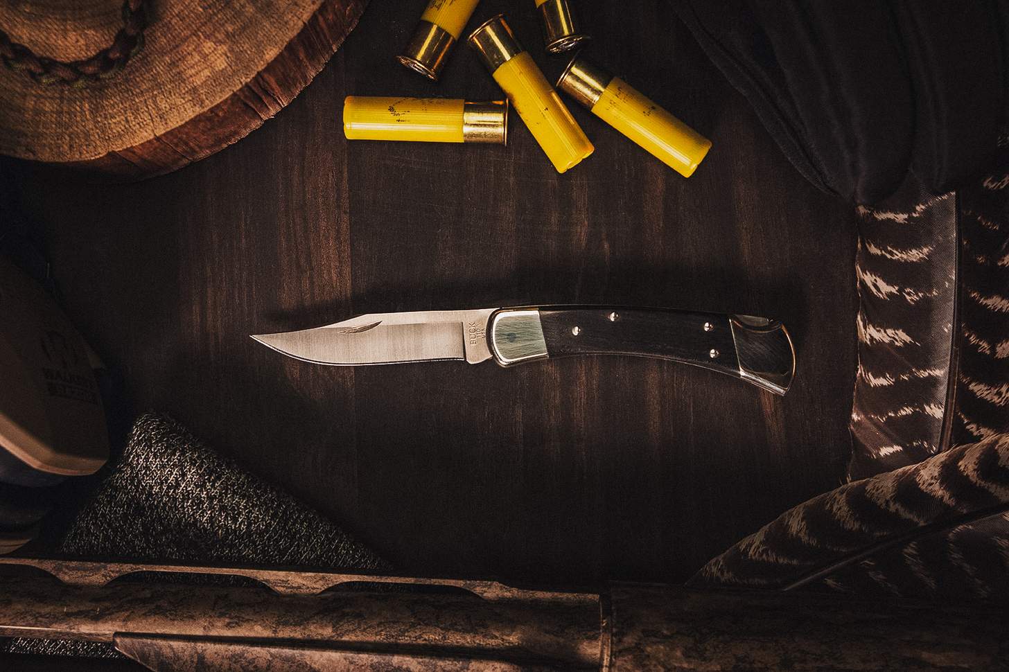 a Buck Knives Buck 110 folding knife on a table with 20 gauge shotshells