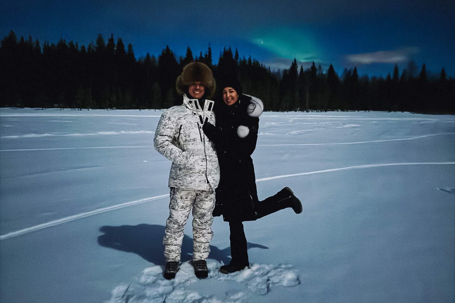 two people standing in the snow with an aurora in the background