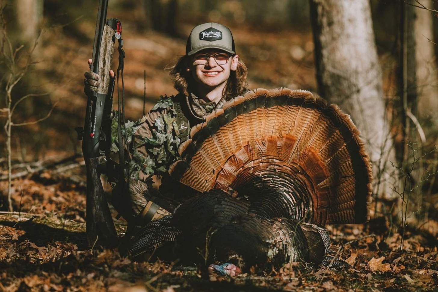 A young hunters poses with a turkey and a shotgun.