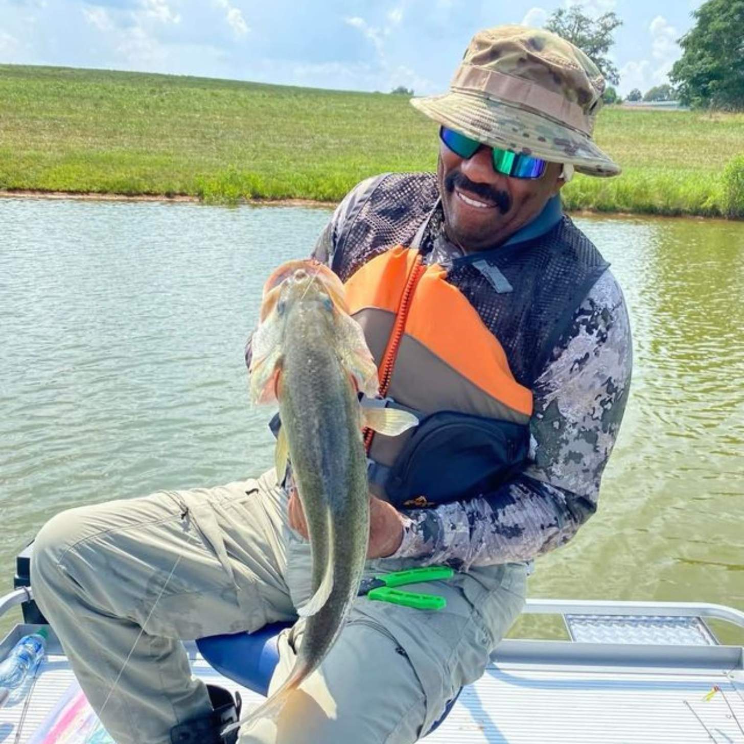 A man in a wide brim hat and sunglasses holds a largemouth bass.