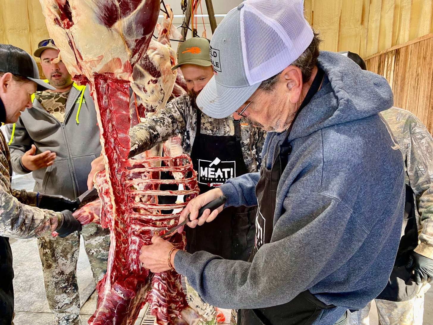 Several men butcher a hanging deer.