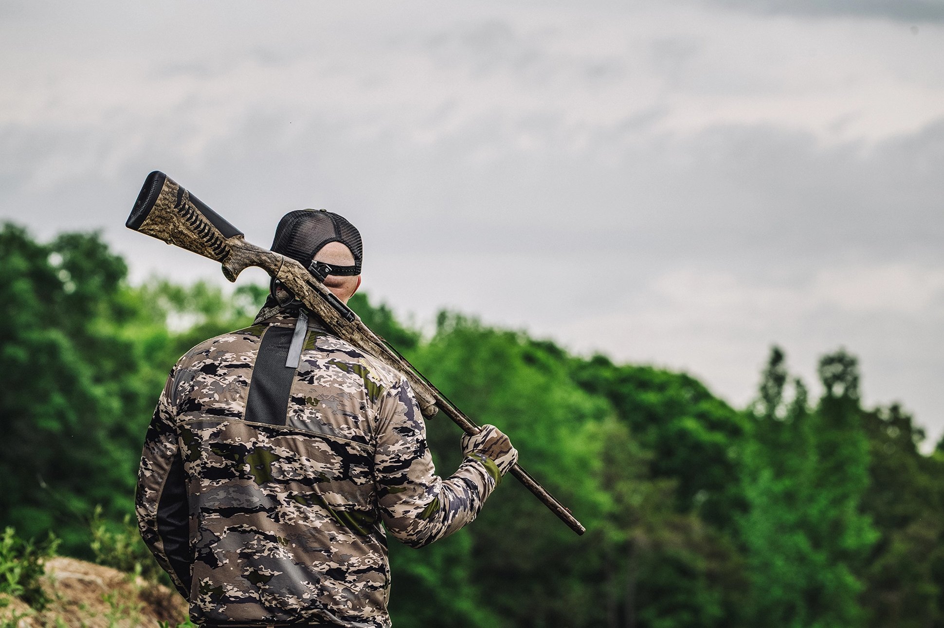 a turky hunter holds his shotgun over his shoulder by the barrel