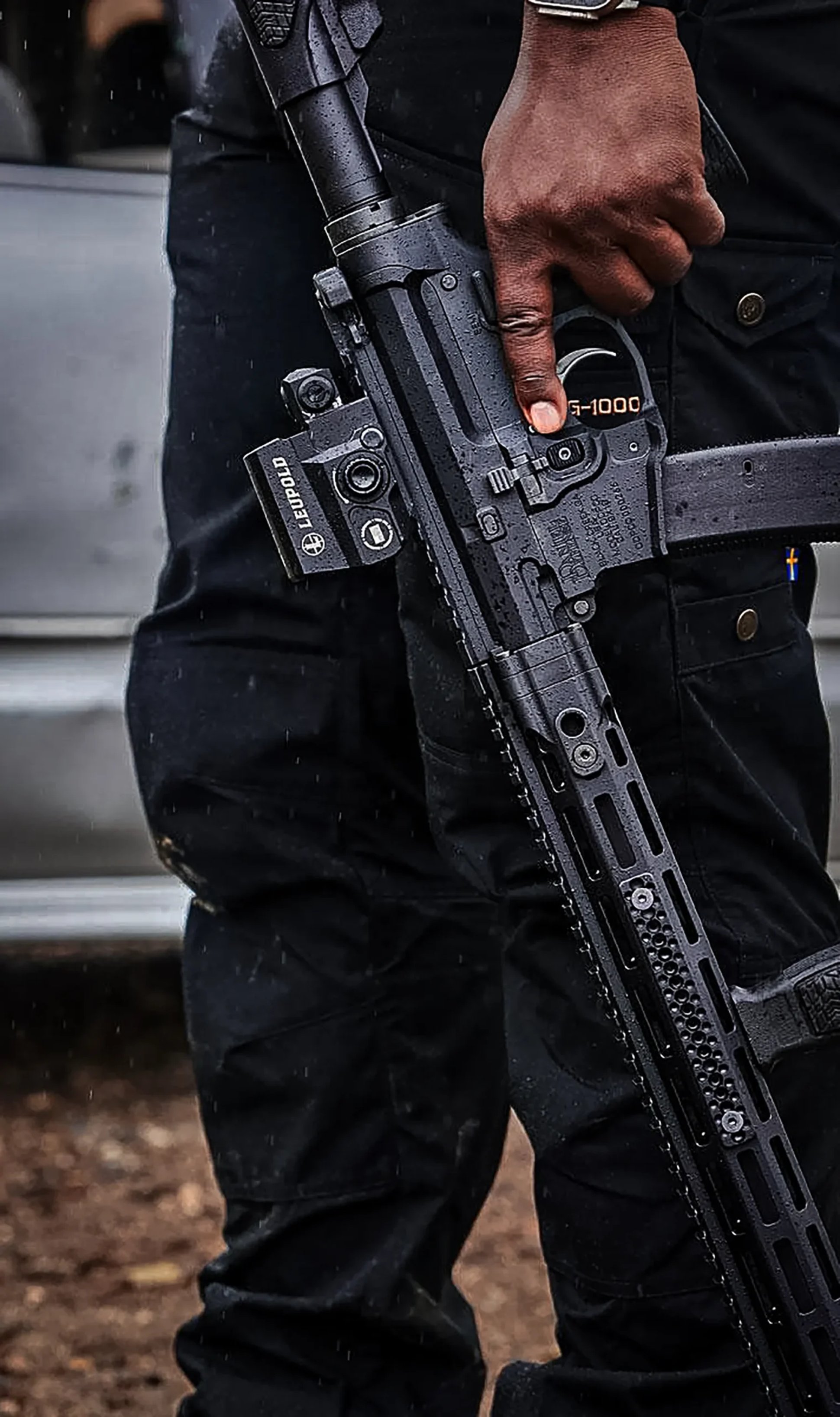 a man holding a Daniel Defense PCC topped with a Leupold red dot at his side