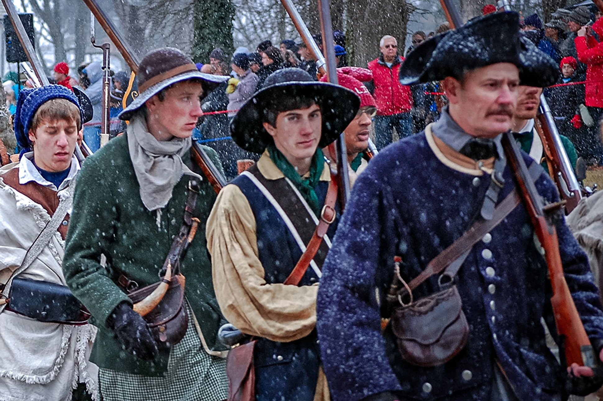 reenactors recreating washington's crossing of the delaware river. The man in the back can be seen wearing a recreation of a liberty cap.