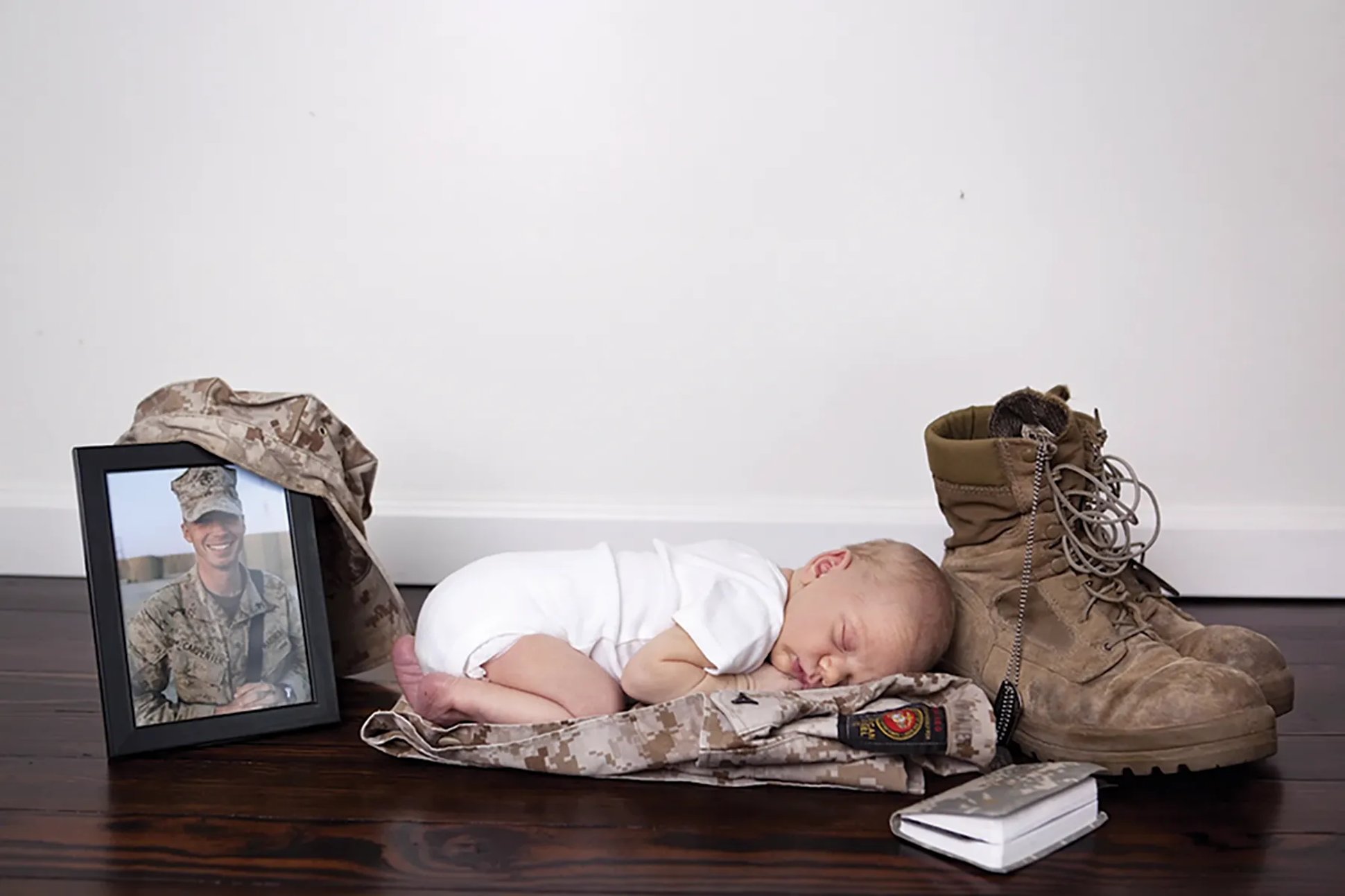 A baby laying on a military uniform between a pair of boots and a photo. Folds of HOnor