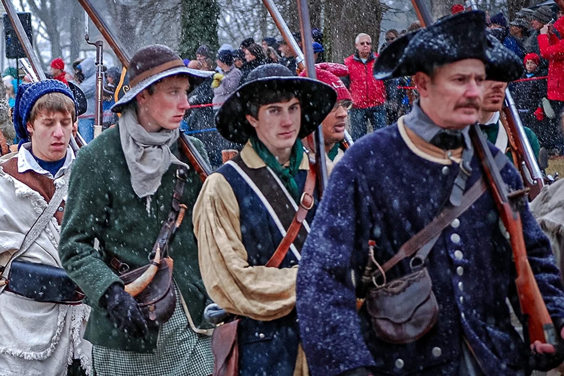 reenactors recreating washington's crossing of the delaware river. The man in the back can be seen wearing a recreation of a liberty cap.